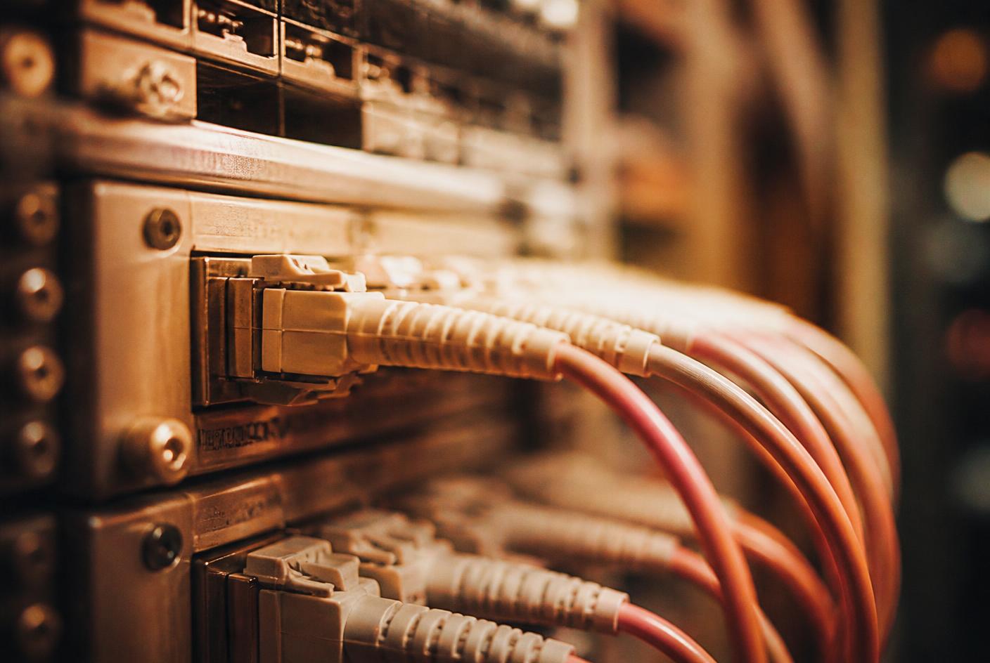 Close-up of fibre optic cables connected into a server rack switch under warm amber lighting